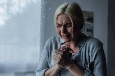 depressed blonde woman crying behind window glass with rain drops 