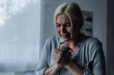 depressed blonde woman crying behind window glass with rain drops  clipart