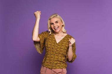 happy blonde woman in blouse having menopause and rejoicing on purple 