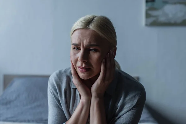 upset blonde woman with menopause touching face and looking away