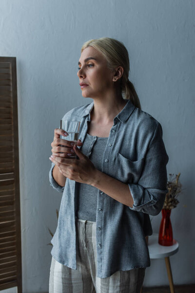 blonde woman with menopause holding glass of water and looking away