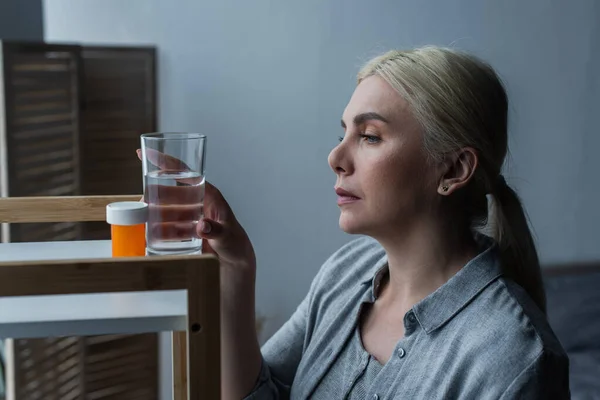 Blonde Woman Menopause Looking Medication Reaching Glass Water Table — Φωτογραφία Αρχείου