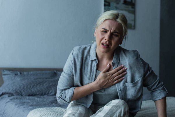 exhausted blonde woman touching chest and feeling pain during menopause 