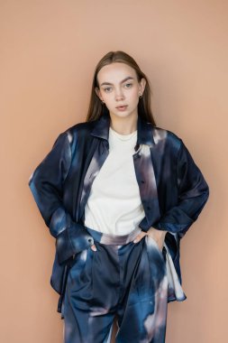 Moda elbisesi içinde genç bir kadın elleri cebinde bej rengi bir elbiseyle dikiliyor.