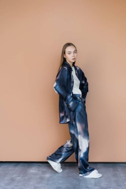 Eğilimli takım elbiseli bir kadın bej arka planda el ele yürüyor.