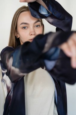Moda eğilimli tişörtlü bir kadın beyaz tenli, bulanık ön planda kameraya bakıyor.