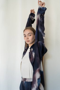 young woman in blue and white gradient shirt posing with raised hands on white background