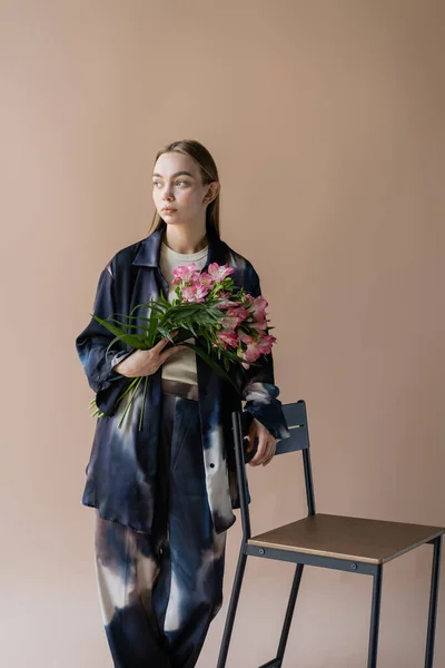 Trendy Woman Alstroemeria Flowers Standing Chair Looking Away Isolated Beige — Foto de Stock