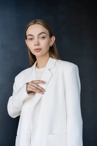 Mulher Elegante Tocando Blazer Branco Olhando Para Câmera Fundo Preto — Fotografia de Stock