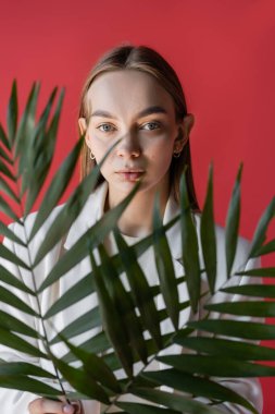 young woman in while clothing holding blurred tropical leaves isolated on crimson