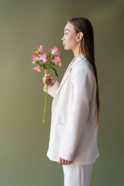 side view of woman in white blazer posing with branch of alstroemeria isolated on green