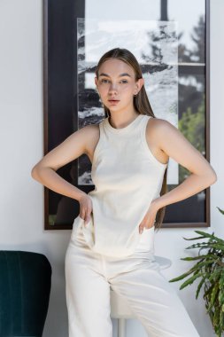 fashionable woman posing with hands in pockets of white tank top 