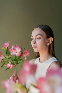 Bulanık ön planda Alstroemeria 'nın dalına bakan büyüleyici kadın yeşilde izole edilmiş.