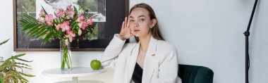 trendy woman looking at camera near ripe apple and bouquet on coffee table, banner