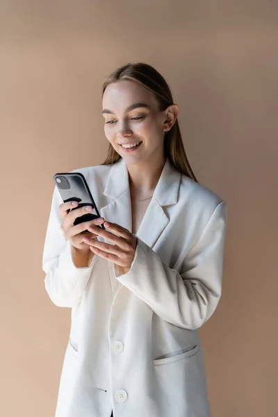 Счастливая Молодая Женщина Белом Блейзере Сообщения Мобильном Телефоне Изолированы Бежевый — стоковое фото