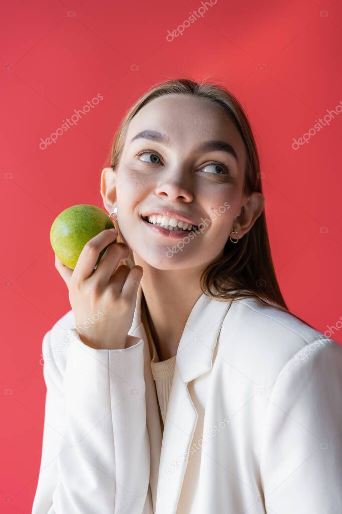smiling woman with fresh ripe apple looking away isolated on carmine pink