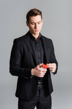 Resmi kıyafetli ciddi bir adam, gri paketten sigara alıyor.