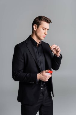 man in black suit holding cigarette and pack isolated on grey