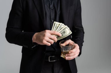 cropped view of man in black formal wear with whiskey and dollars isolated on grey clipart