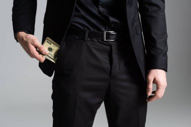cropped view of man in black suit holding money near pocket isolated on grey clipart