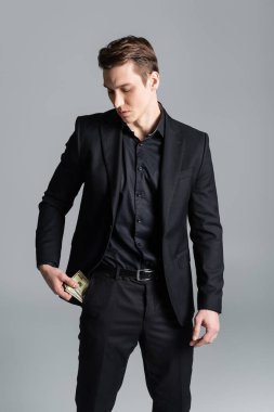 stylish man in black formal wear getting money out of pocket isolated on grey