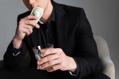 cropped view of blurred man with dollars and glass of whiskey isolated on grey clipart