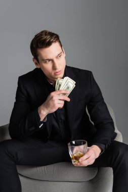 Viski ve para dolu banknotları olan düşünceli bir adam griye bakıyor.