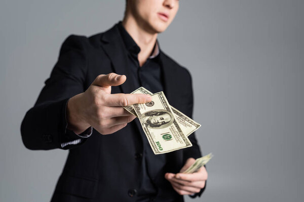 partial view of blurred man holding dollar banknotes isolated on grey