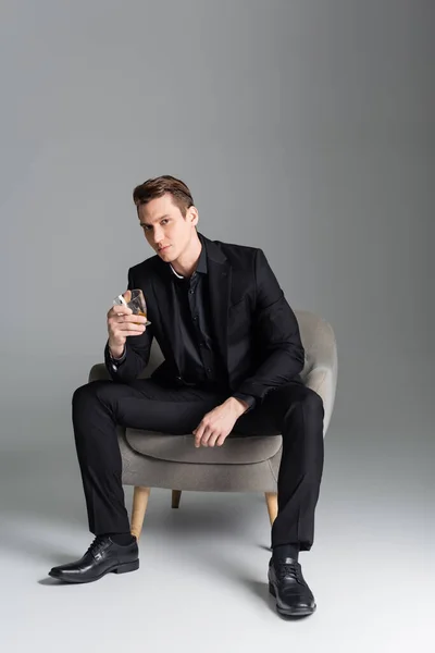 Full Length Stylish Man Glass Whiskey Sitting Armchair Grey Background — Stok fotoğraf