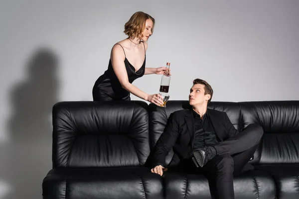 Sexy Woman Glass Bottle Whiskey Man Sitting Black Couch Grey — 스톡 사진