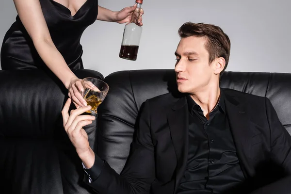 Woman Proposing Whiskey Man Black Clothes Sitting Leather Sofa Isolated — Stockfoto