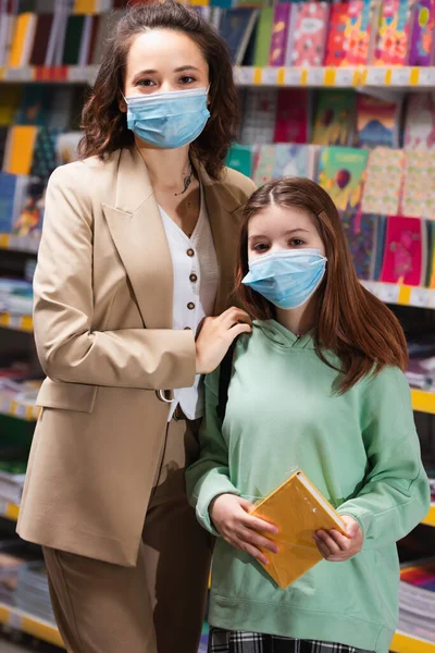 Mother Daughter Medical Masks Looking Camera Blurred Rack Colorful Copybooks — Stock Photo, Image