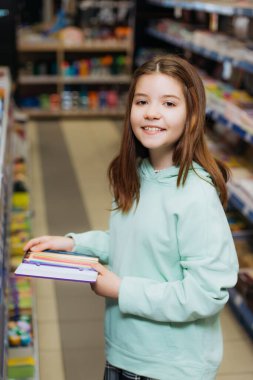 happy girl with set of color pencils looking at camera in stationery shop