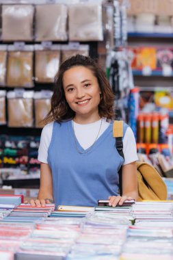 young and happy woman looking at camera near copybooks in stationery shop