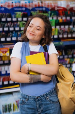 pleased student with closed eyes hugging new copybooks in stationery store