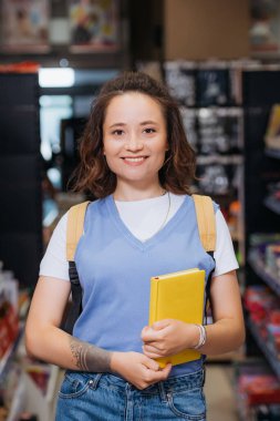 young woman with new copybook smiling at camera in stationery shop