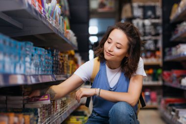 tattooed student choosing paper notes on rack in stationery store