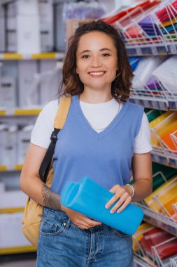 happy young woman with plastic files and backpack looking at camera in stationery store