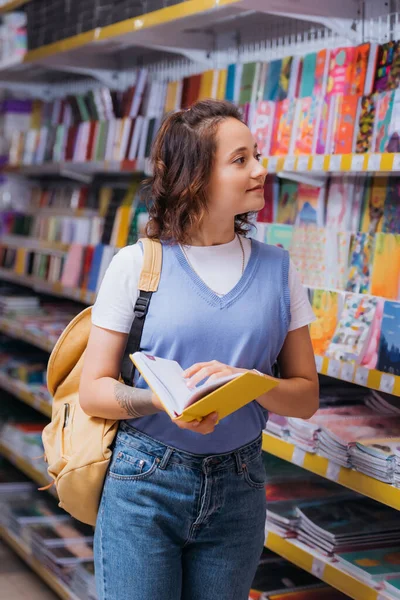Sırt Çantalı Pozitif Öğrenci Kırtasiye Dükkanında Kitaplarla Rafa Bakıyor — Stok fotoğraf