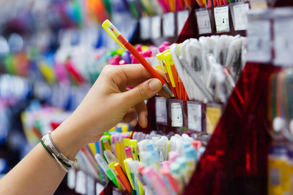 partial view of woman in beaded bracelets holding colorful ball pen near rack with stationery