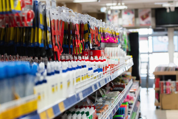 different scissors and glue on rack with school supplies in stationery store