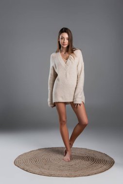 full length of slender woman with naked legs standing on carpet on grey background