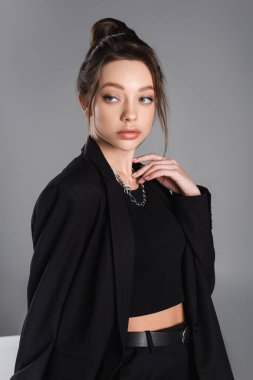 pretty woman in black jacket and silver necklace looking away isolated on grey