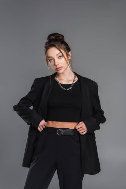 pretty woman in black suit and crop top posing with hands on waist isolated on grey