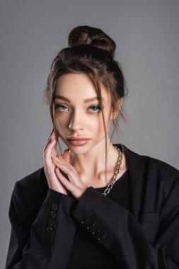 portrait of stylish woman with makeup looking at camera and touching face isolated on grey