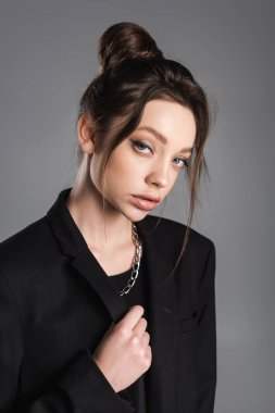 pretty woman with makeup and silver necklace looking at camera isolated on grey