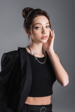 pretty woman in black clothes touching face and looking at camera isolated on grey