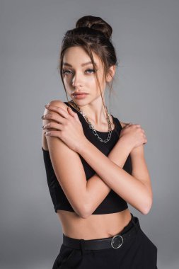 trendy woman with makeup and silver necklace posing with crossed arms isolated on grey