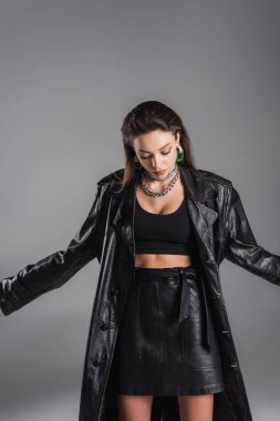 young brunette woman in leather skirt and black coat isolated on grey