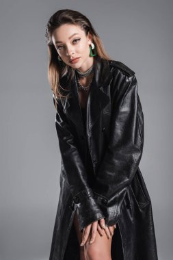 pretty young woman in trendy leather coat looking at camera isolated on grey